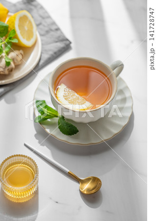Cup of tea with lemon, ginger, honey and mint on a marble background with citrus fruits Cup of tea with lemon, ginger, honey and mint on a marble background with citrus fruits 141728747