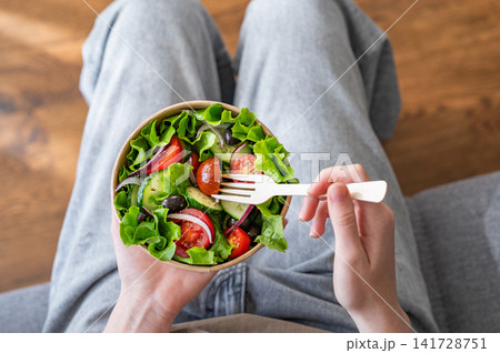 A woman holds a healthy vegetable salad in an eco-friendly takeaway bowl. A woman holds a healthy vegetable salad in an eco-friendly takeaway bowl. 141728751