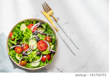 A fresh salad of tomatoes, cucumbers, lettuce, red onions, and olives on a marble background A fresh salad of tomatoes, cucumbers, lettuce, red onions, and olives on a marble background 141728755