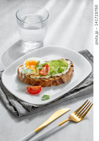 Avocado toast with egg, cream cheese, tomatoes, and basil on a concrete background Avocado toast with egg, cream cheese, tomatoes, and basil on a concrete background 141728760