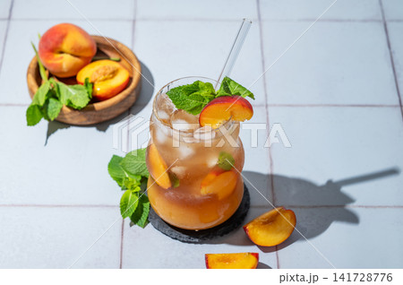 Refreshing peach iced cocktail or tea with mint in a glass on a tile background with shadow. Refreshing peach iced cocktail or tea with mint in a glass on a tile background with shadow. 141728776