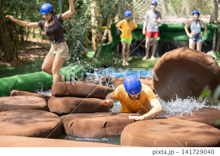 Guys and girl walking through water obstacle course in summer adventure park Guys and girl walking through water obstacle course in summer adventure park 141729040