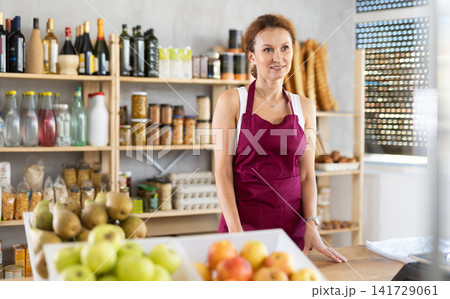 Portrait of positive female salesperson behind supermarket counter. Interior of grocery supermarket 141729061