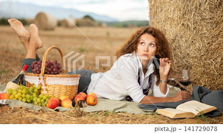 Woman in white blouse in office clothes, lying on blanket and reading book. Picnic on farm field Woman in white blouse in office clothes, lying on blanket and reading book. Picnic on farm field 141729078