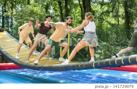 Group trying to cross moving swinging bridge over trampoline Group trying to cross moving swinging bridge over trampoline 141729079