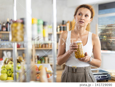 Female shopper carefully choosing jar of canned olives in grocery supermarket Female shopper carefully choosing jar of canned olives in grocery supermarket 141729090