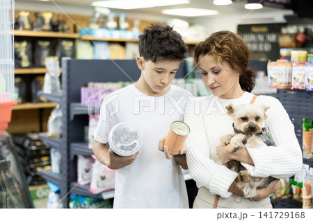 Mother with dog Yorkshire Terrier in arms and son carefully examine label on dry dog food Mother with dog Yorkshire Terrier in arms and son carefully examine label on dry dog food 141729168