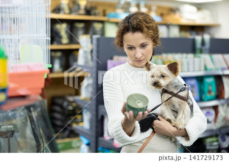 Female owner of Yorkshire terrier choosing canned dog food in pet store Female owner of Yorkshire terrier choosing canned dog food in pet store 141729173