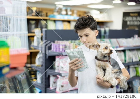 Boy with dog Yorkshire terrier in arms and read composition of product at packaging of dog dry food Boy with dog Yorkshire terrier in arms and read composition of product at packaging of dog dry food 141729180