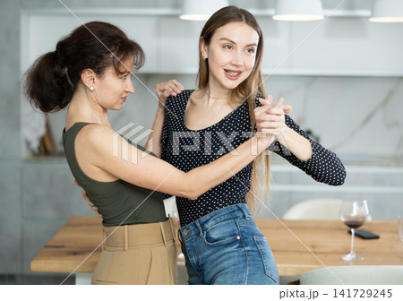 Two joyful middle-aged women dancing together at the kitchen-table with wineglasses Two joyful middle-aged women dancing together at the kitchen-table with wineglasses 141729245
