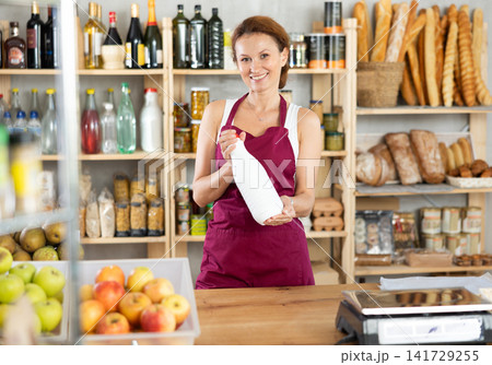 Adult woman seller offers milk in grocery store 141729255