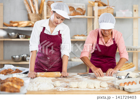 Female bakers rolling out dough and shaping pastries in bakery Female bakers rolling out dough and shaping pastries in bakery 141729403
