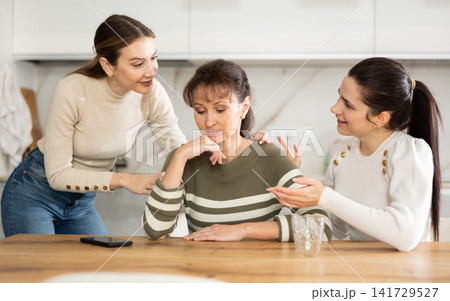 Sad middle-aged woman sitting at table while two others trying to calm her Sad middle-aged woman sitting at table while two others trying to calm her 141729527