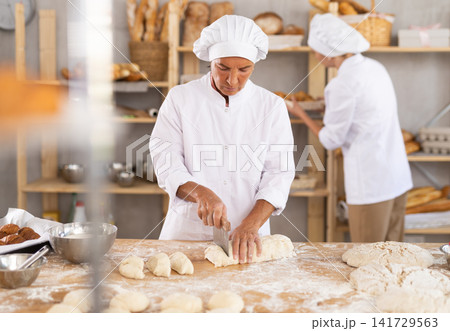 Experienced female baker portioning dough on floured table Experienced female baker portioning dough on floured table 141729563