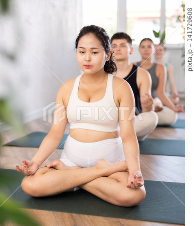 Young yogi girl and man making yoga meditation in lotus pose in fitness studio 141729608