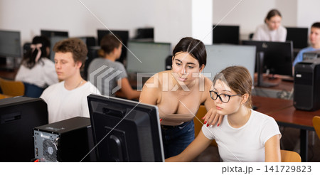 Focused female teenager helping to the positive classmate while she is learning computer science in the class Focused female teenager helping to the positive classmate while she is learning computer science in the class 141729823