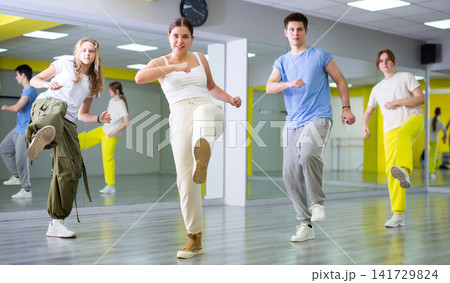 Confident sporty teens moving their foot right into camera while exercising dance together in hall Confident sporty teens moving their foot right into camera while exercising dance together in hall 141729824