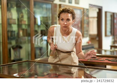 Woman examining antique artifacts within glass vitrine in museum Woman examining antique artifacts within glass vitrine in museum 141729832