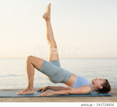 Near sea during sunset, girl performs Setu Badha Sarvangasana Near sea during sunset, girl performs Setu Badha Sarvangasana 141729838