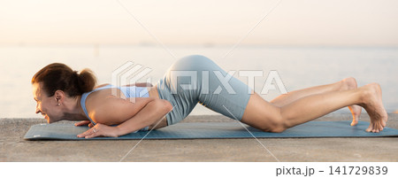 Sportive woman performing cobra pose of yoga during training on beach at sunrise Sportive woman performing cobra pose of yoga during training on beach at sunrise 141729839