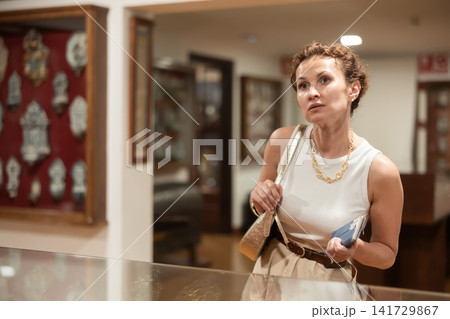 Interested woman examining collection of artifacts in historical museum Interested woman examining collection of artifacts in historical museum 141729867