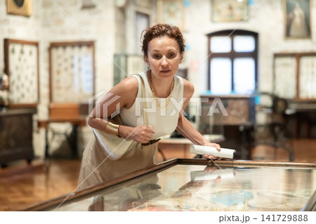 Woman examining antique artifacts within glass vitrine in museum Woman examining antique artifacts within glass vitrine in museum 141729888