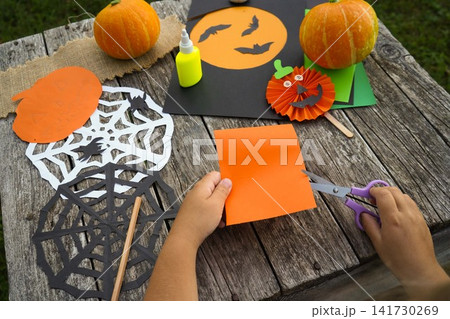 Close up of a child using purple safety scissors to cut out shapes from a bright orange paper sheet Close up of a child using purple safety scissors to cut out shapes from a bright orange paper sheet 141730269