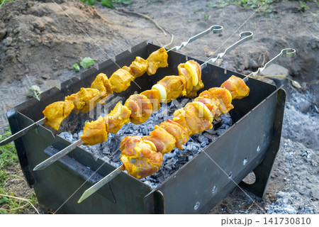 raw meat kebab on skewers cooking on metal barbecue grill with coals 141730810