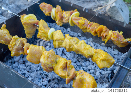 close up of raw marinated meat on skewers over coals in barbecue grill 141730811