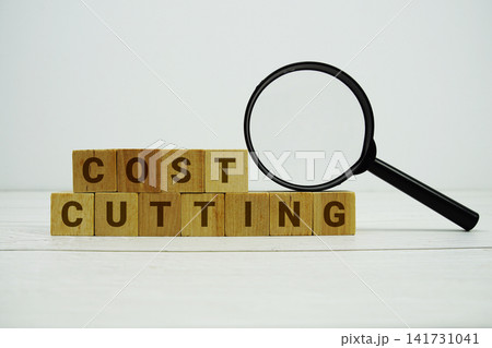 COST CUTTING alphabet letters with magnifying glass on wooden background COST CUTTING alphabet letters with magnifying glass on wooden background 141731041