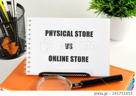A notebook on a desk shows the words physical store vs online store. A pen and a magnifying glass sit nearby, with a plant in the background A notebook on a desk shows the words physical store vs online store. A pen and a magnifying glass sit nearby, with a plant in the background 141731055