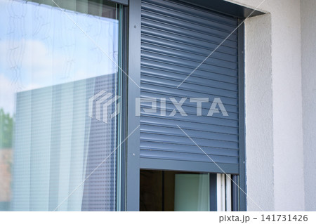 Roller shutter is partly closed over an exterior window on a modern house Roller shutter is partly closed over an exterior window on a modern house 141731426