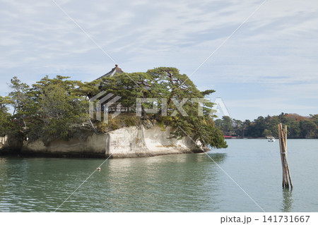 A serene scene at Matsuyama, featuring a traditional Japanese pavilion perched on the edge of a rocky island surrounded by calm waters under a soft blue sky with wispy clouds. A serene scene at Matsuyama, featuring a traditional Japanese pavilion perched on the edge of a rocky island surrounded by calm waters under a soft blue sky with wispy clouds. 141731667