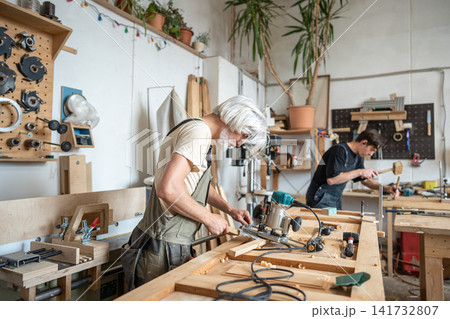 Concentrated master technician setting up handheld wood router instrument for work in workshop. 141732807