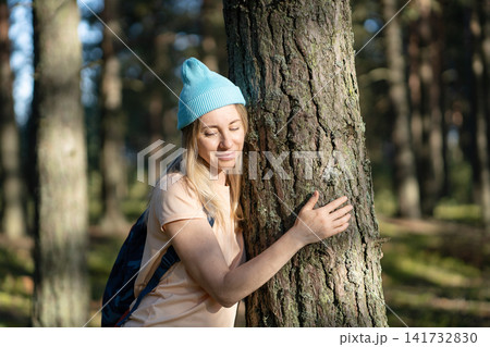 Calm woman standing in forest and hugging big tree trunk at sunset, loving nature, relieving stress 141732830