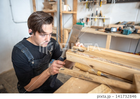Attentive craftsman woodworker carefully cutting off old damaged part of wood from board with saw. 141732846