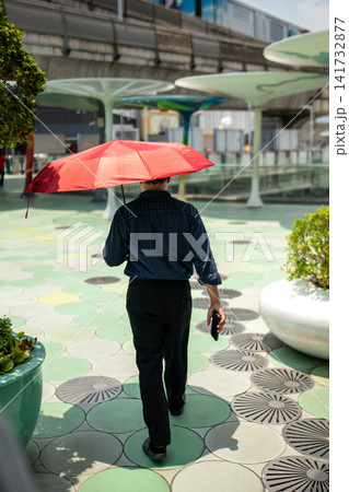 Unrecognizable man hiding under protective red umbrella from immense heat and sunlight while walking on hot day on street. 141732877