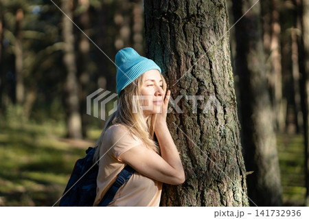 Carefree mature woman hiking in forest alone, standing lean to tree enjoying peaceful moment. Carefree mature woman hiking in forest alone, standing lean to tree enjoying peaceful moment. 141732936