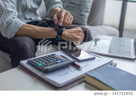 Professional checking smartwatch notifications while analyzing budget with calculator and laptop. Professional checking smartwatch notifications while analyzing budget with calculator and laptop. 141732958