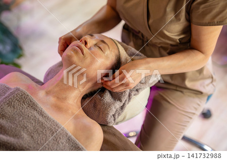 Tranquil woman on spa table receiving skin care treatment and healing massage procedure in salon. Tranquil woman on spa table receiving skin care treatment and healing massage procedure in salon. 141732988