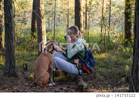 Positive woman forager having lunch break during active forest walk and foraging together with dog. Positive woman forager having lunch break during active forest walk and foraging together with dog. 141733122