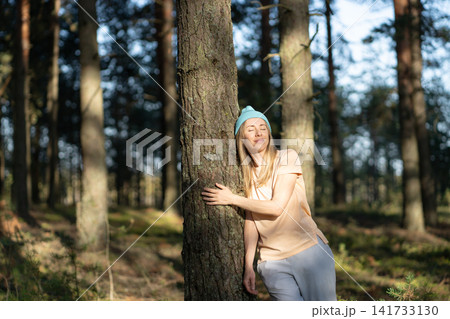 Carefree smiling woman hiking in forest alone, standing lean to tree enjoying peaceful moment. 141733130