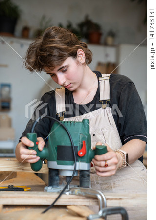 Talented concentrated woman restorer working in restoration workshop with electric router tool. 141733131