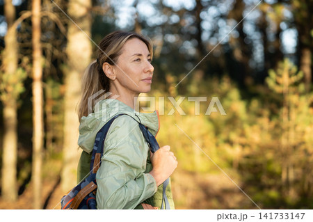 Confident positive woman hiking in forest with backpack, standing looking at sun enjoying quiet rest Confident positive woman hiking in forest with backpack, standing looking at sun enjoying quiet rest 141733147