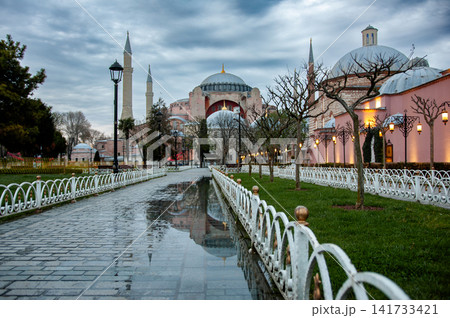 Hagia Sophia and its minaret reflected in a calm garden pool with a white railing at dusk in Istanbul, Turkey, a peaceful view of the historic landmark. Hagia Sophia and its minaret reflected in a calm garden pool with a white railing at dusk in Istanbul, Turkey, a peaceful view of the historic landmark. 141733421