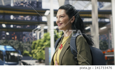 Close up of upbeat woman holding mobile phone while moving in bus station waiting area. Joyful female passenger route information on smartphone, walking to coach platform Close up of upbeat woman holding mobile phone while moving in bus station waiting area. Joyful female passenger route information on smartphone, walking to coach platform 141733476