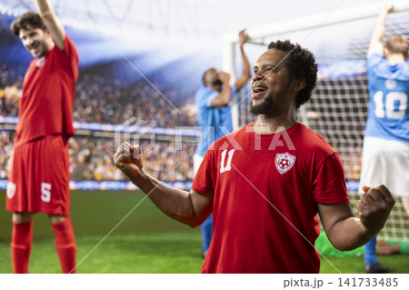 African american red soccer player smiling and celebrating with clenched fists during goal celebration near goal net, joyful reaction on pitch. Red team excitement and win. 141733485