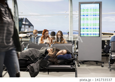 Bored girl resting in airport using phone to tell family about arriving late home for holidays. Annoyed woman in departure terminal using smartphone to text boyfriend about flight delay 141733537