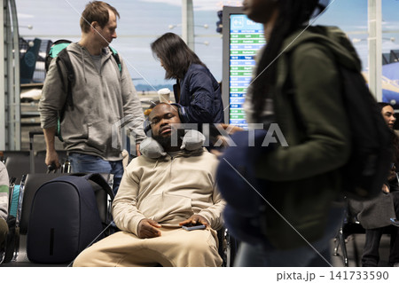 Sleeping, neck pillow and tired man in airport waiting in lounge during delayed flights. Napping, headphones and exhausted african american person on chair in airport terminal during holiday trip 141733590