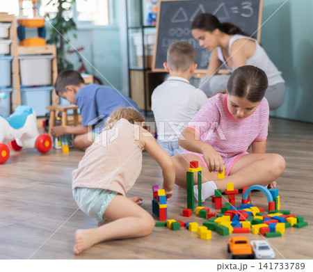 Little children sitting on floor together and playing educational games and toys at classes for kids Little children sitting on floor together and playing educational games and toys at classes for kids 141733789
